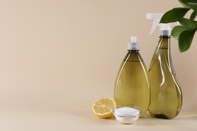 Photo of Bottles of cleaning product, lemon and baking soda on beige background. Space for text