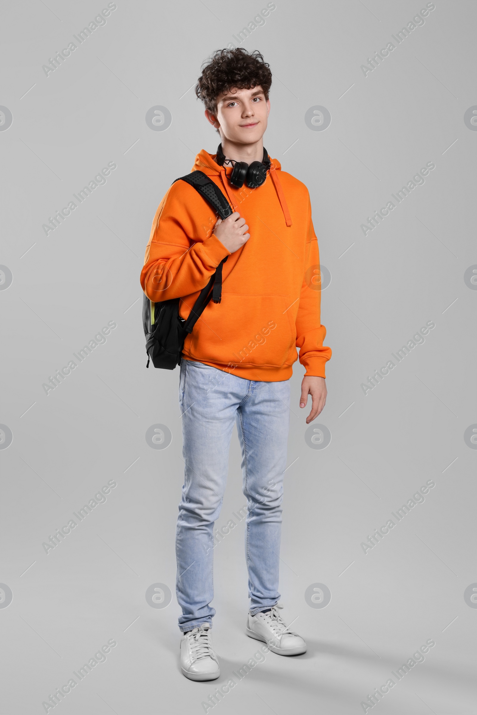 Photo of Teenage boy with headphones and backpack on light grey background