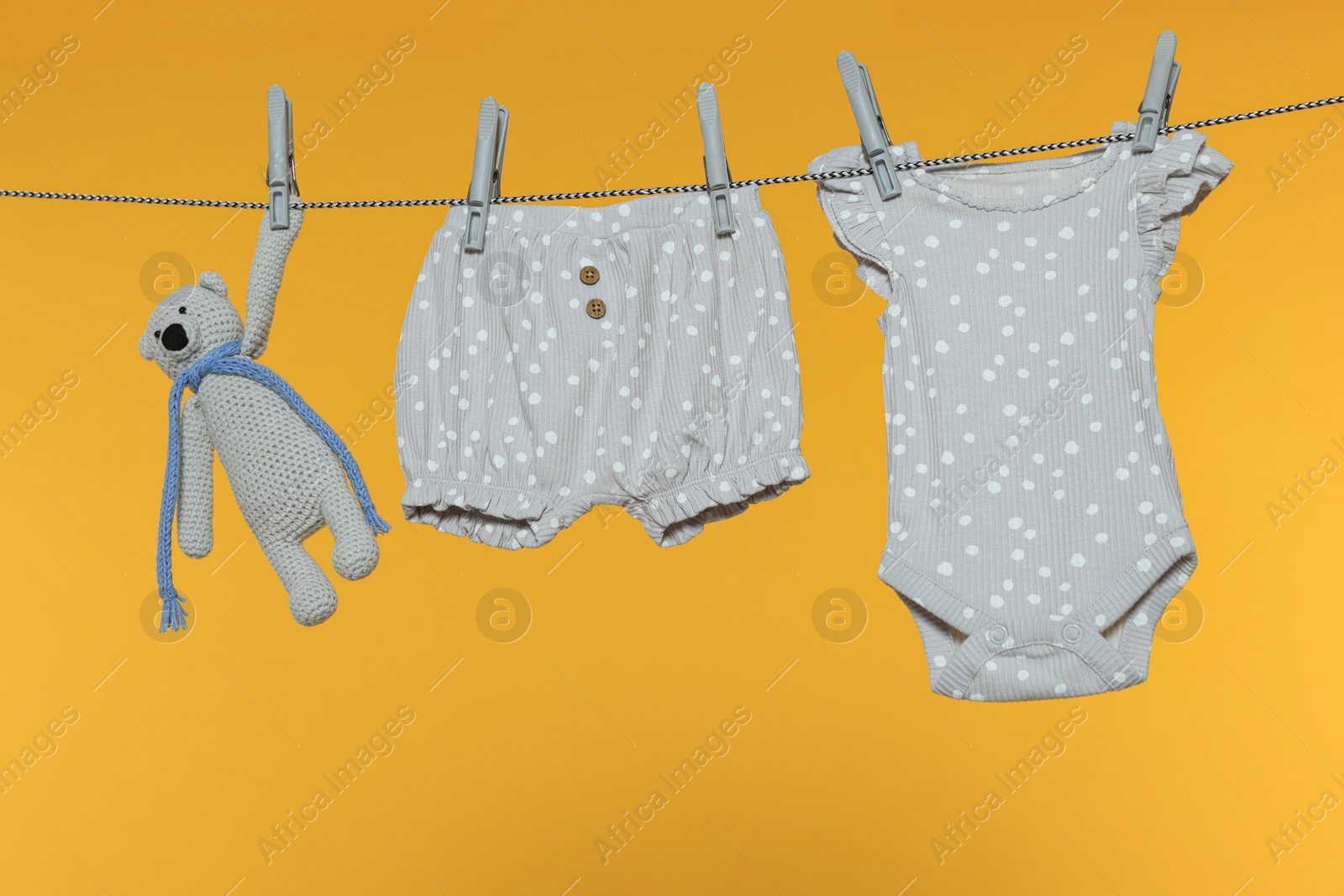 Photo of Baby clothes and bear toy drying on laundry line against orange background