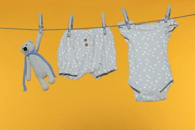 Baby clothes and bear toy drying on laundry line against orange background