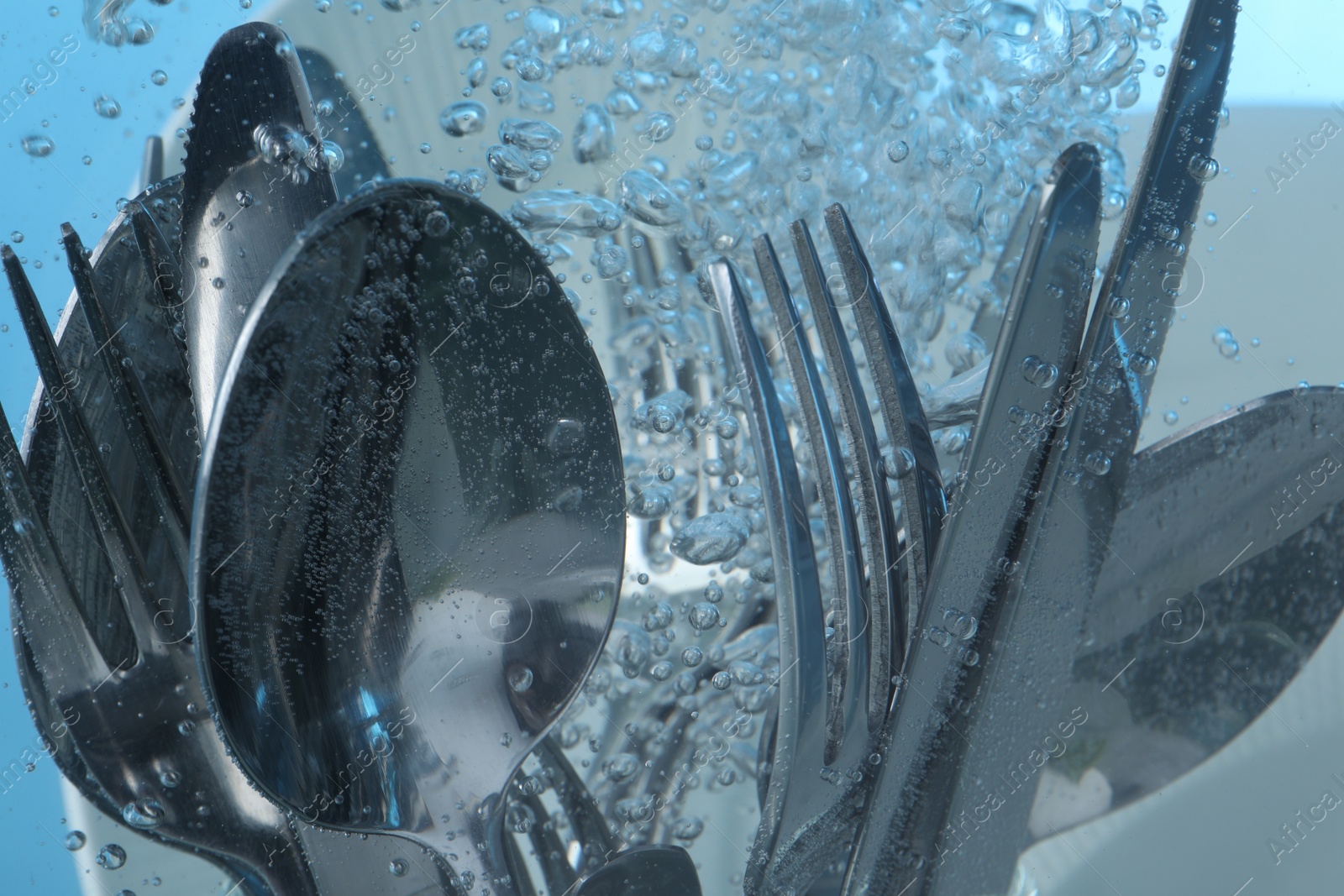 Photo of Washing silver cutlery in water on light blue background, closeup