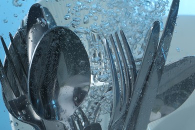 Photo of Washing silver cutlery in water on light blue background, closeup