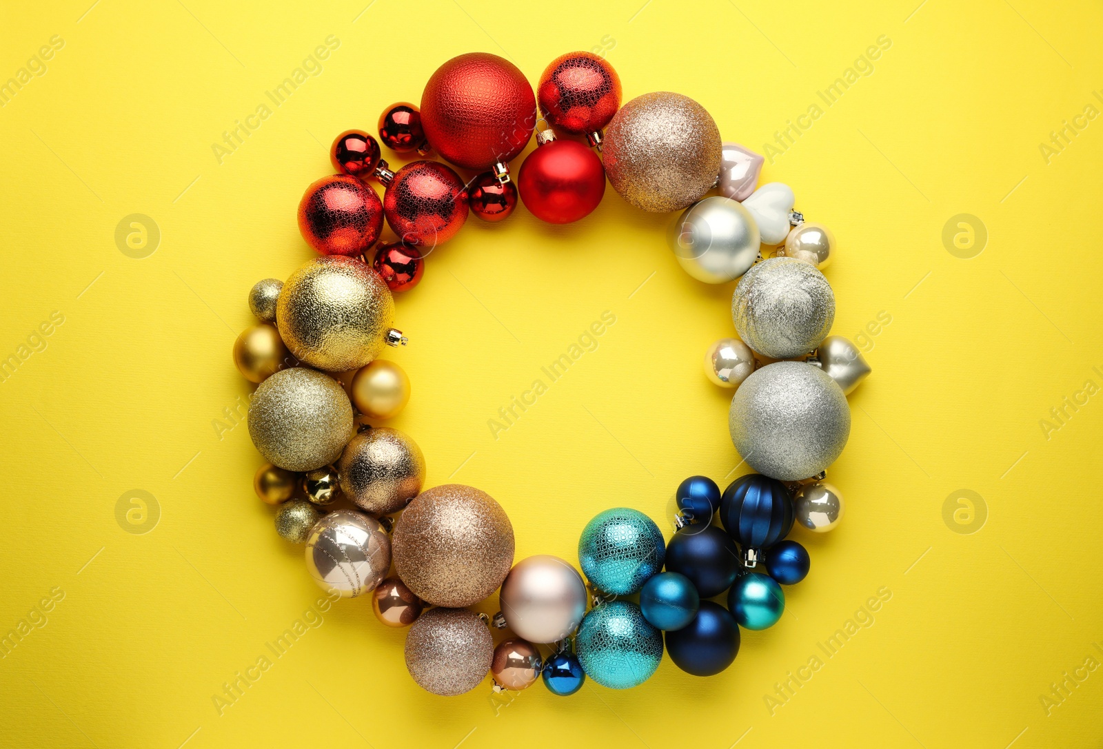 Photo of Bright festive wreath made of Christmas balls on yellow background, top view. Space for text