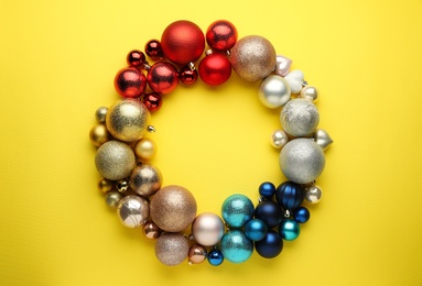 Bright festive wreath made of Christmas balls on yellow background, top view. Space for text