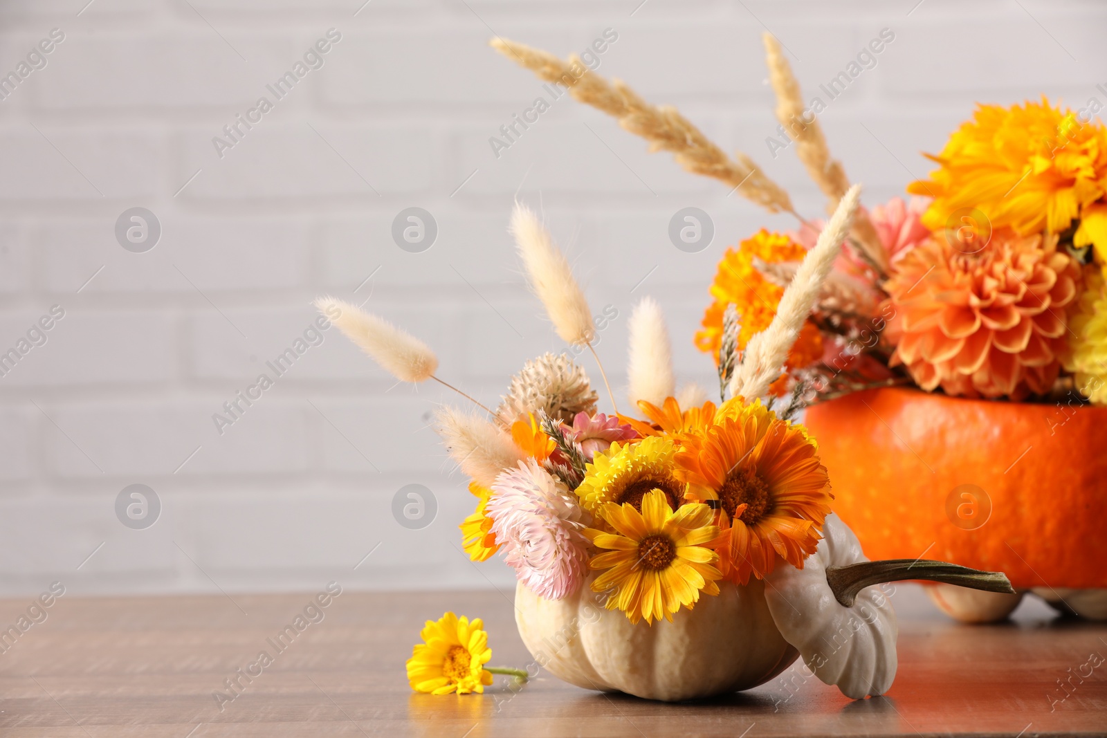 Photo of Decorative pumpkins with beautiful flowers and spikelets on wooden table against white brick wall, closeup. Space for text