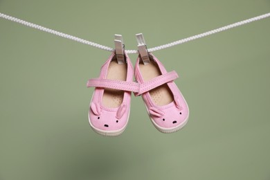 Photo of Cute small baby shoes hanging on washing line against green background