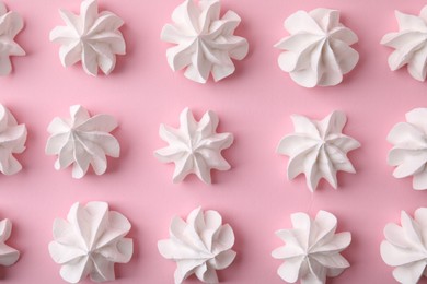 Many tasty meringue cookies on pink background, flat lay