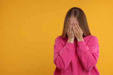 Resentful woman covering face with hands on orange background, space for text