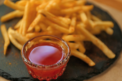 Photo of Delicious hot french fries with red sauce served on table, closeup