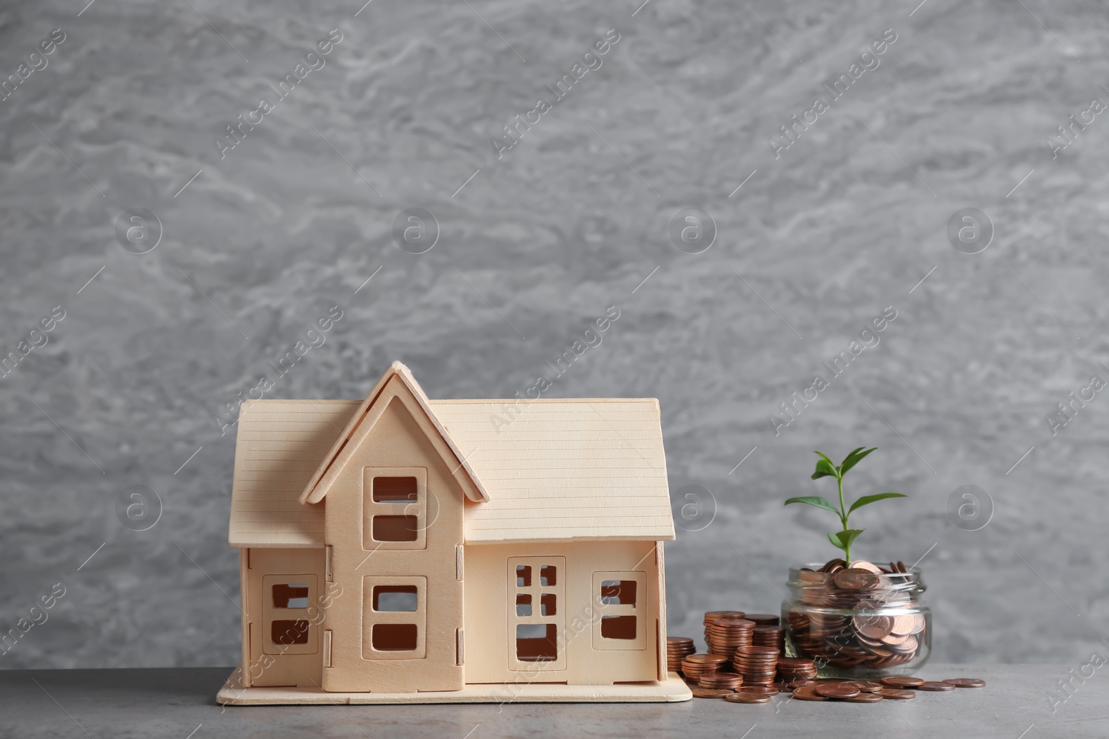 Photo of House model and jar with coins on table against grey background. Space for text