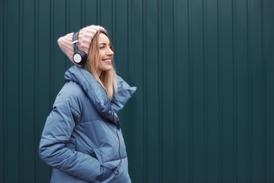 Photo of Young woman with headphones listening to music near color wall. Space for text
