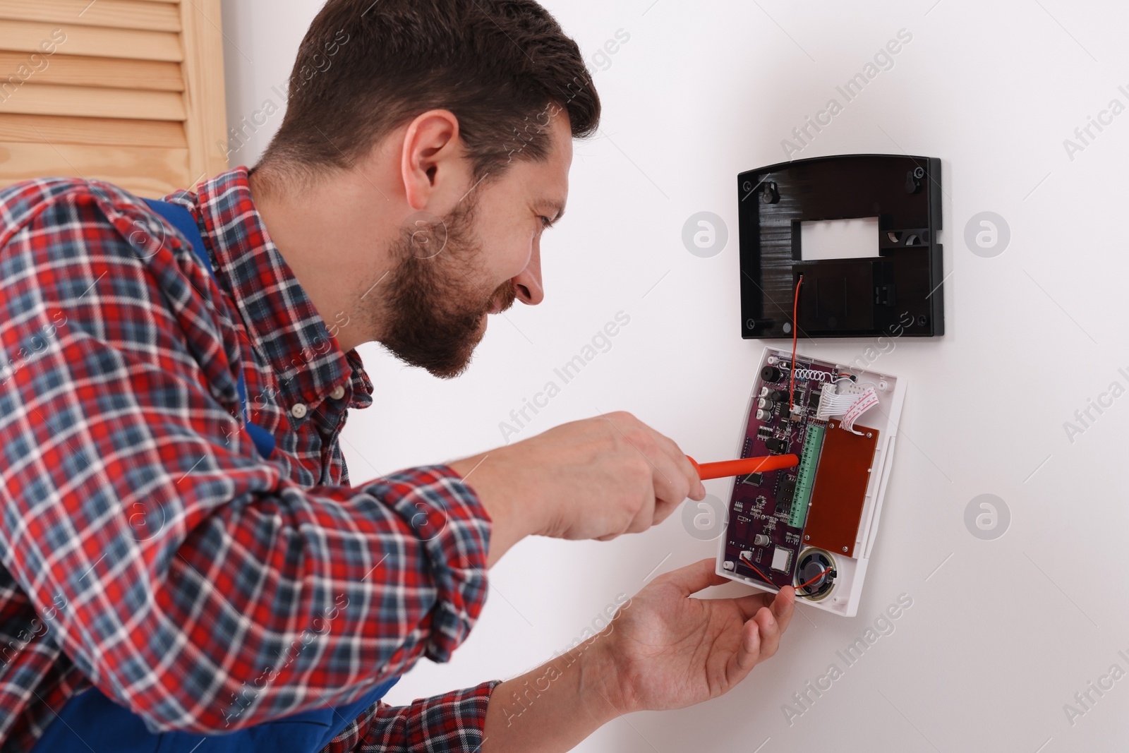 Photo of Technician installing home security alarm system on white wall indoors