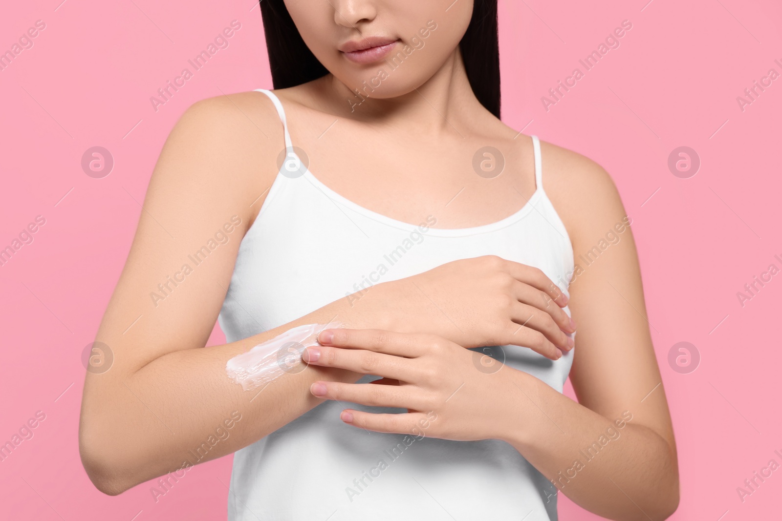 Photo of Young woman applying body cream onto arm on pink background, closeup