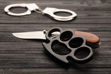 Photo of Brass knuckles, knife and handcuffs on black wooden background
