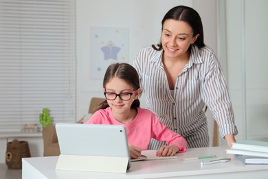 Photo of Mother helping her daughter doing homework with tablet at home