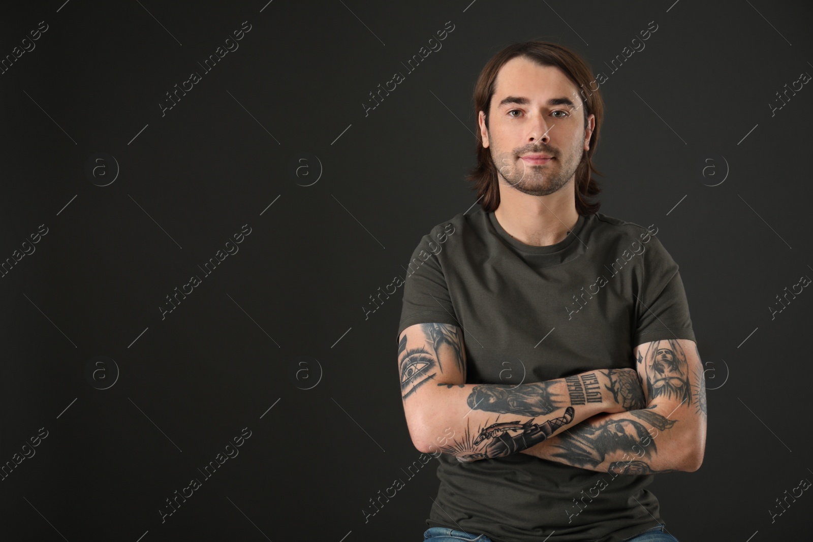 Photo of Young man with tattoos on arms against black background. Space for text