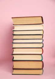 Stack of different hardcover books on pink background