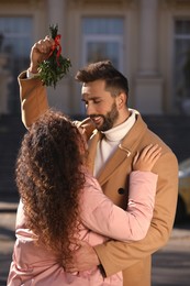 Happy couple under mistletoe bunch outdoors. Christmas tradition