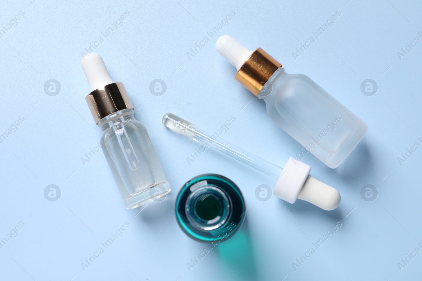 Photo of Bottles of cosmetic serum on light blue background, flat lay