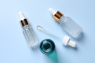 Bottles of cosmetic serum on light blue background, flat lay