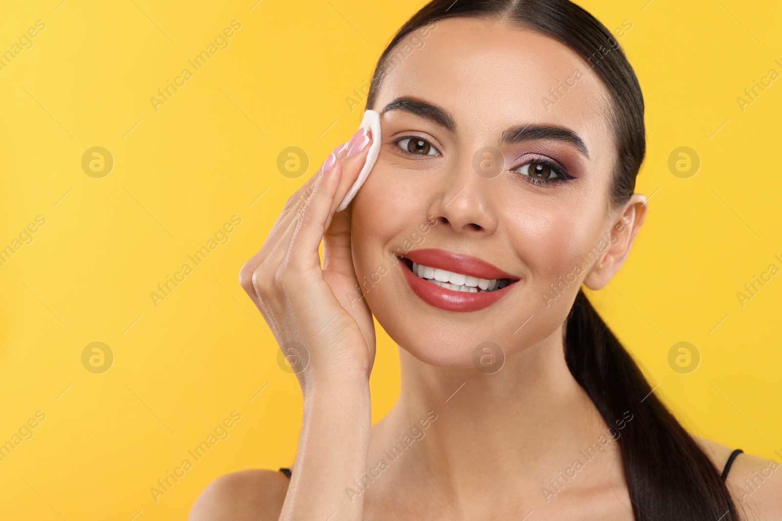 Photo of Beautiful woman removing makeup with cotton pad on orange background, space for text