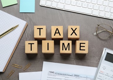 Flat lay composition of wooden cubes with words Tax Time and documents on grey table