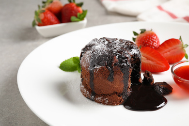 Photo of Delicious warm chocolate lava cake with mint and strawberries on plate, closeup