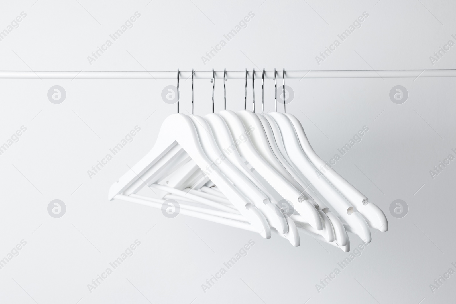 Photo of White clothes hangers on metal rail against light background