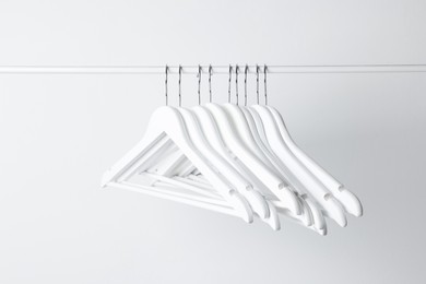 Photo of White clothes hangers on metal rail against light background