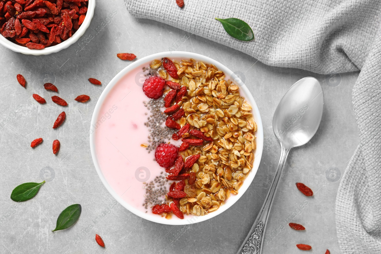 Photo of Smoothie bowl with goji berries on grey table, flat lay