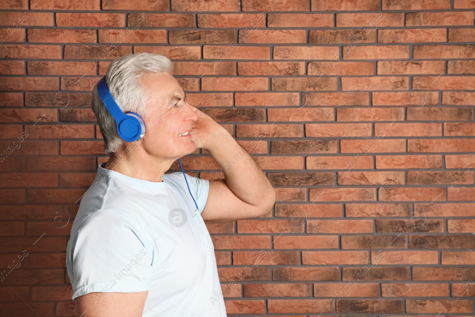 Photo of Mature man enjoying music in headphones against brick wall. Space for text