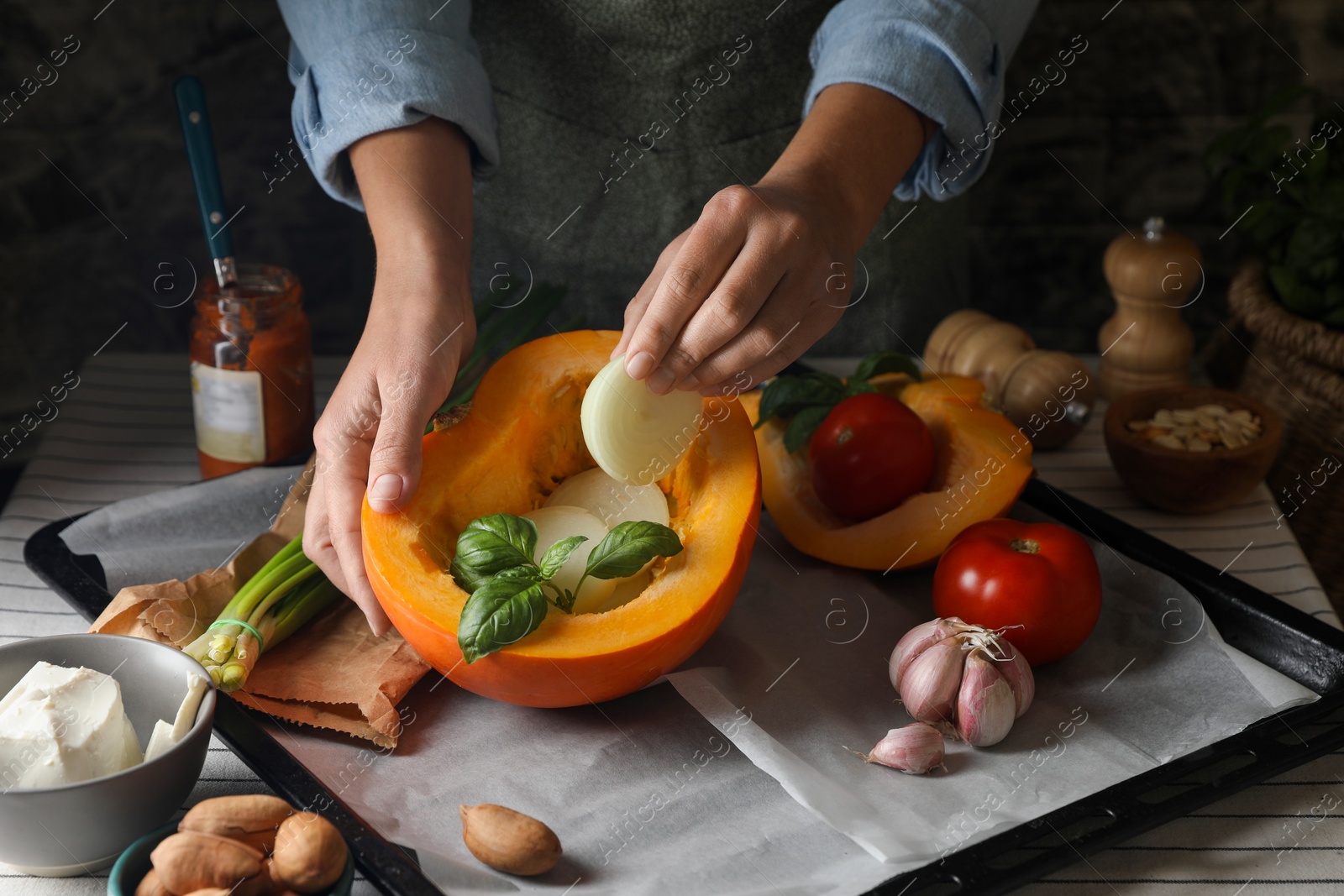 Photo of Woman stuffing pumpkin with vegetables at table, closeup