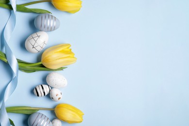 Flat lay composition with tulips and beautifully painted eggs on light blue background, space for text. Easter celebration