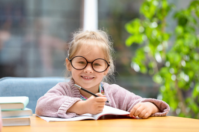 Photo of Cute little girl studying at wooden table indoors