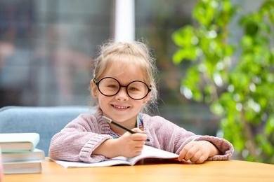 Cute little girl studying at wooden table indoors