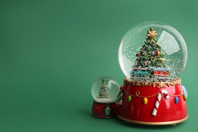 Photo of Beautiful snow globes with Christmas trees on green background, space for text