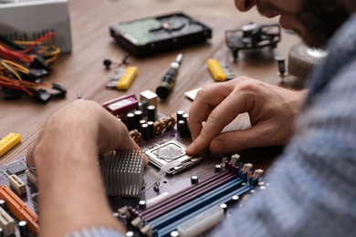 Photo of Male technician repairing motherboard at table, closeup