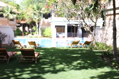 Photo of Blurred view of backyard with sun loungers on green grass near swimming pool