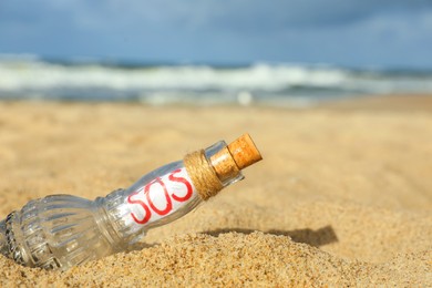 Photo of Glass bottle with SOS message on sand near sea, closeup