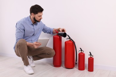 Photo of Man with tablet checking fire extinguishers indoors