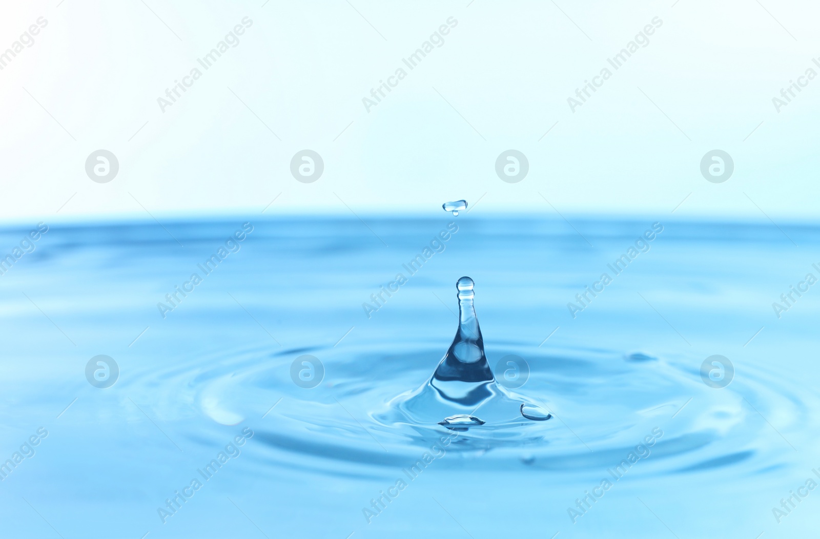 Photo of Splash of clear water with drop on light blue background, closeup