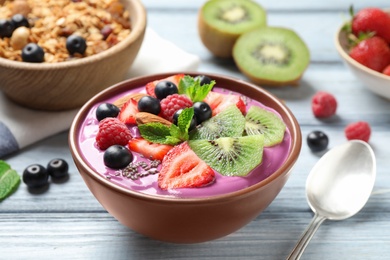 Photo of Delicious acai smoothie with chia seeds and fruits in dessert bowl served on white wooden table