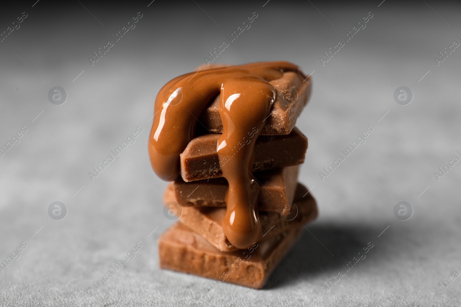 Photo of Pieces of milk chocolate with tasty paste on gray table, closeup