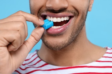 Happy man with bubble gum on light blue background, closeup