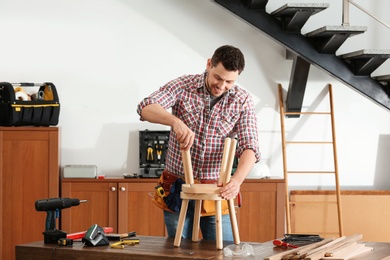 Handsome working man repairing wooden stool indoors