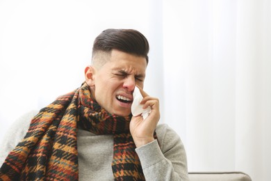 Photo of Ill man with scarf suffering from head cold at home