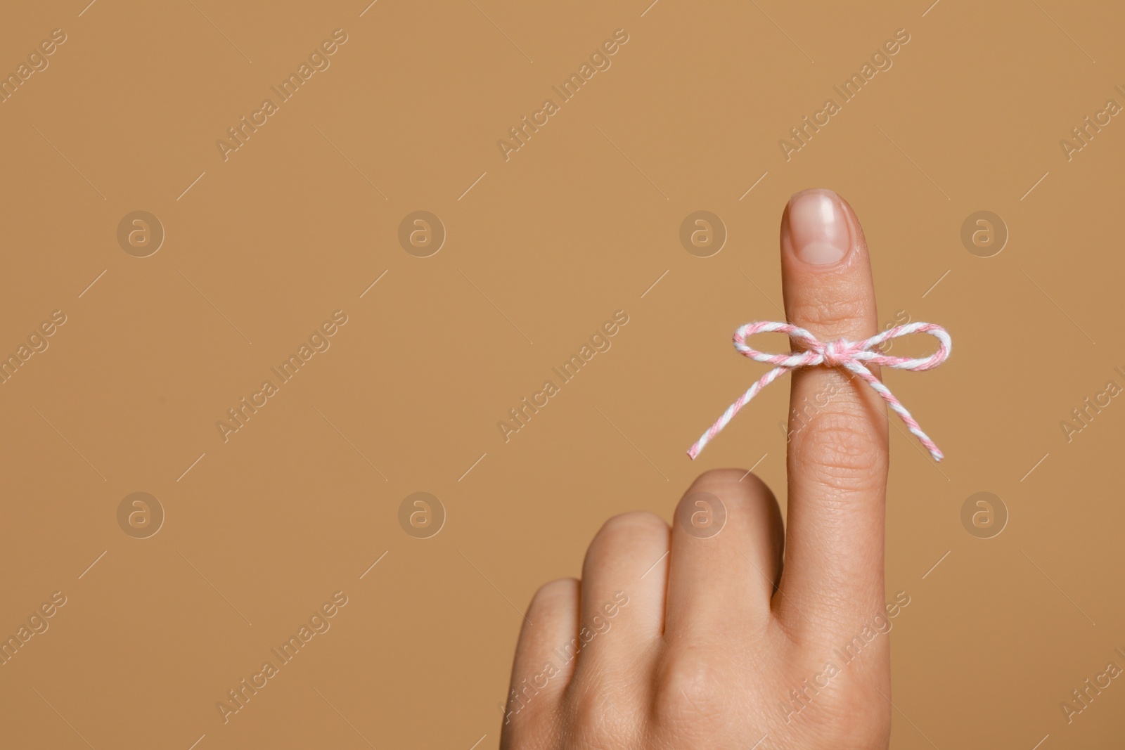 Photo of Woman showing index finger with tied bow as reminder on light brown background, closeup. Space for text