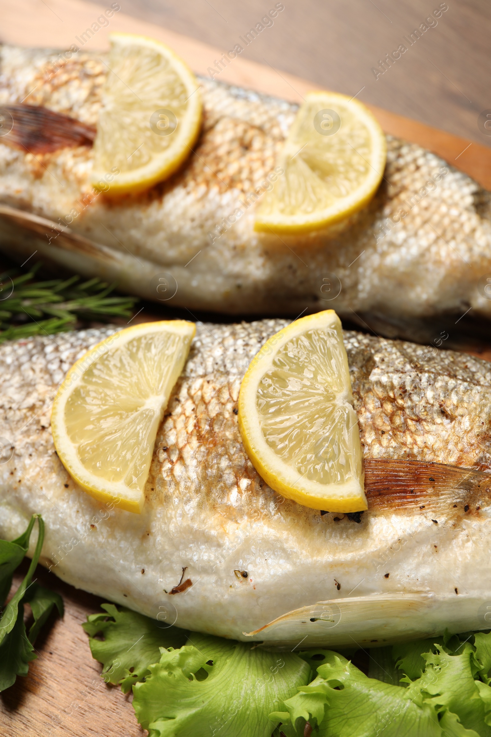 Photo of Delicious baked fish, lettuce and lemon on table, closeup