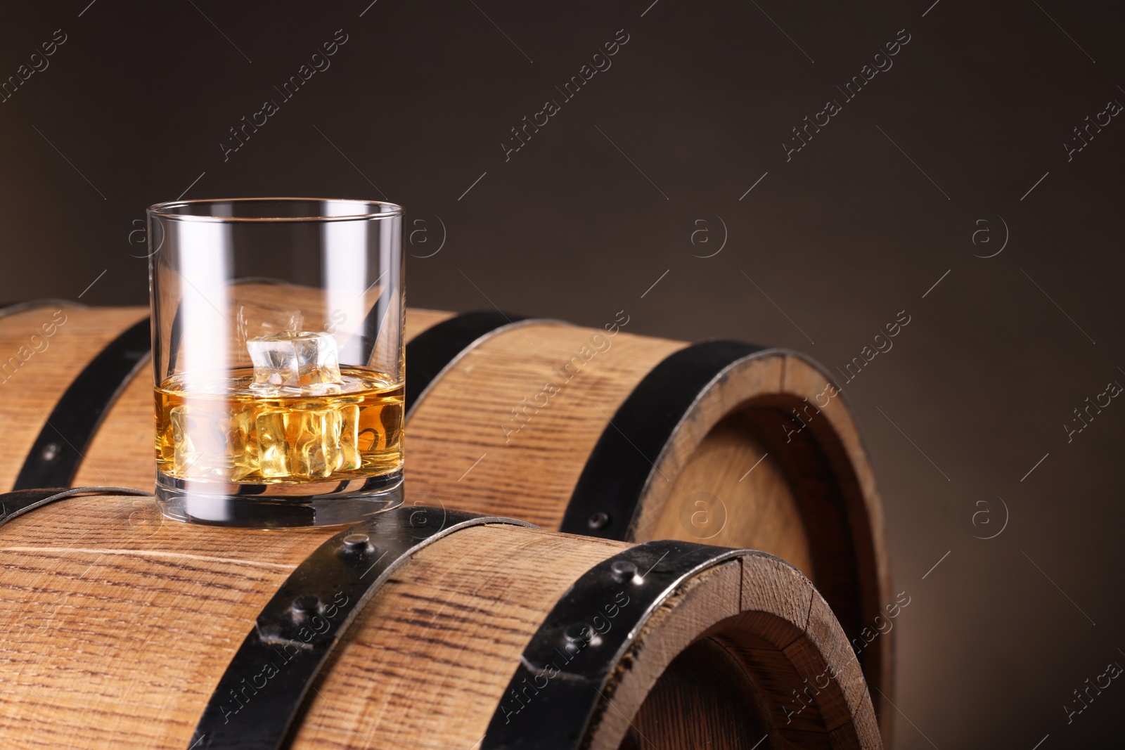 Photo of Whiskey with ice cubes in glass on wooden barrel against dark background