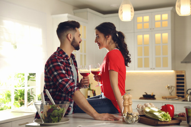 Photo of Lovely young couple drinking wine while cooking together at kitchen